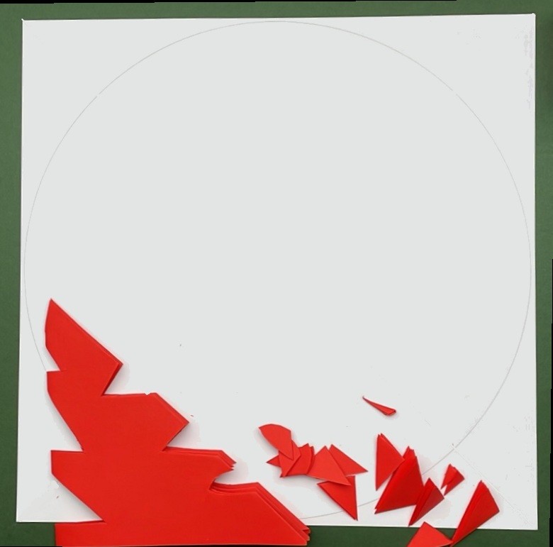 Biała kwadratowa kartka z narysowanym centralnie maksymalnie dużym okręgiem. Na białej kartce złożona trzykrotnie czerwona kartka papieru z wyciętymi na krawędziach trójkątami. Elementy odcięte też leżą obok.